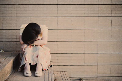 Rear view of girl sitting on floor against wall