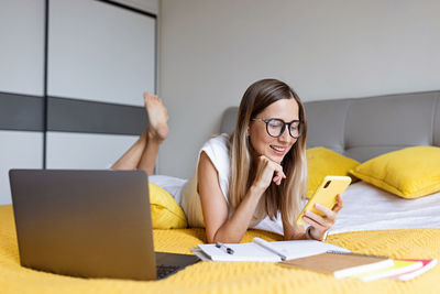 Smiling woman using mobile phone lying on bed