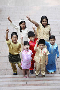 Portrait of cute friends in traditional clothing pointing while standing on footpath