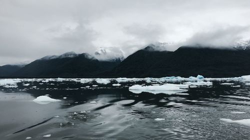 Scenic view of lake by snowcapped mountains against sky