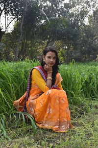 Portrait of smiling young woman sitting by grass outdoors