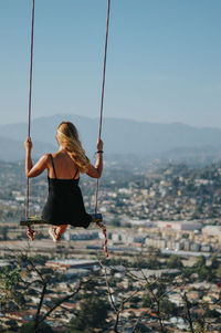 Rear view of woman on swing against clear sky