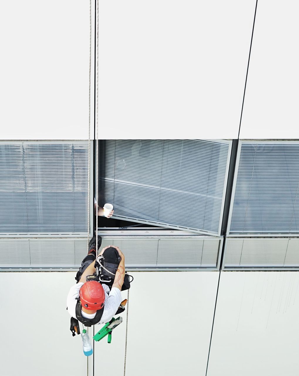 LOW ANGLE VIEW OF MEN ON GLASS WINDOW AGAINST BUILDING