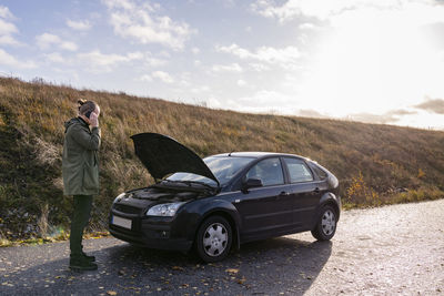 Man using cell phone in front of broken down car