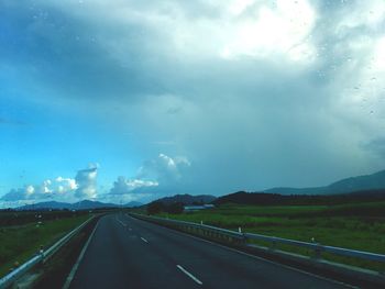 Road passing through landscape against storm clouds