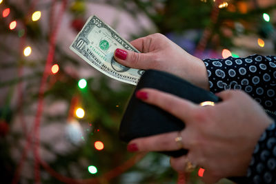 Cropped hands of woman holding paper currency against christmas tree