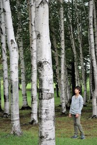 Full length of boy standing on field amidst tree trunk in forest