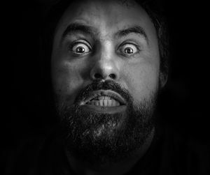 Close-up portrait of angry man with beard against black background