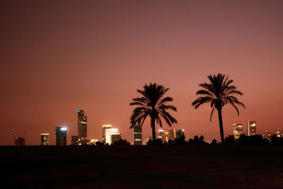 Silhouette palm trees and buildings against sky at sunset