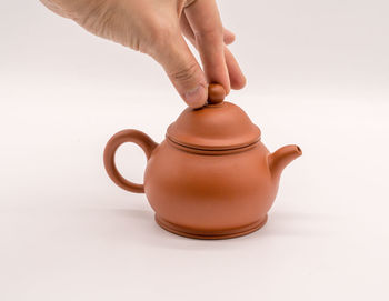 Close-up of human hand holding tea cup against white background