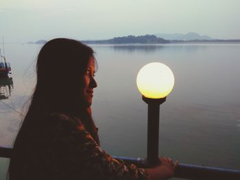 Reflection of woman in lake against sky during sunset