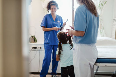 Healthcare workers looking at girl standing in medical examination room