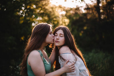 Young woman kissing her girlfriend on the cheek in forest in summer