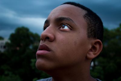 Close-up of teenage boy looking up against cloudy sky
