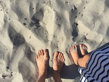 Low section of mother and child standing on sand during sunny day