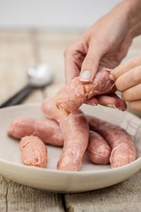 Cropped image of hand holding peeling sausage in bowl