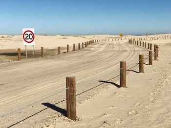 Road sign by dirt road against clear sky