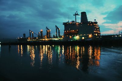 Illuminated factory by building against sky at night