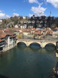 Bridge over river by buildings in city against sky