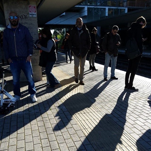 men, lifestyles, large group of people, person, leisure activity, walking, city life, medium group of people, togetherness, transportation, standing, sunlight, full length, casual clothing, street, travel, indoors, shadow, public transportation