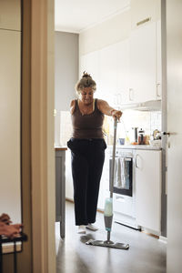 Mature woman with disability mopping kitchen floor at home