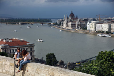 People sitting on bridge over river in city