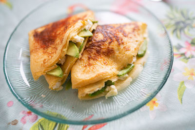 A plate of pancakes with cheese and avocado is on the table with a colorful tablecloth