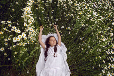 Girl child lies on a camomile field in a white dress in summer