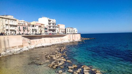 Buildings by sea against clear blue sky