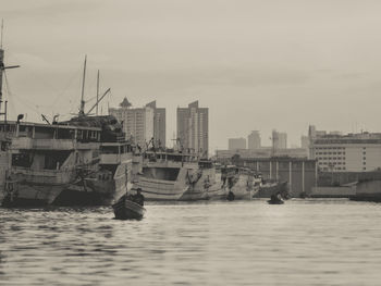 Sailboats moored on sea by buildings in city against sky