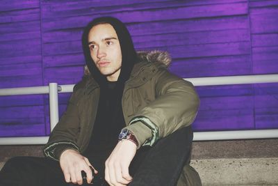 Young man wearing jacket against purple wall