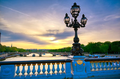 Ferris wheel by river against sky at sunset
