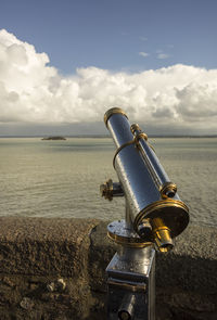 Close-up of coin-operated binoculars by sea against sky