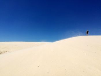 Man on sand dune in desert against clear blue sky