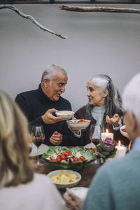 Male and female friends holding food bowls while talking at dinner party