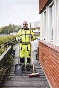 Portrait of smiling man holding broom and equipment