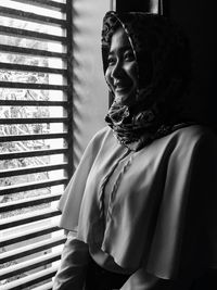 Smiling young woman looking through window at home