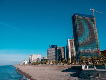 Modern buildings by sea against clear blue sky