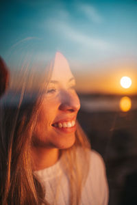 Portrait of smiling young woman against sunset sky