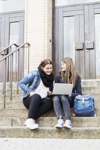 Young female friends using laptop on steps outside school building