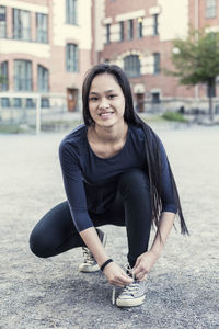 Full length portrait of female student tying shoelace on high school schoolyard