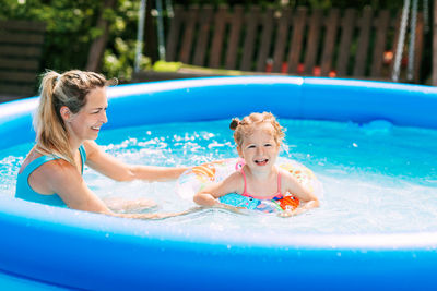 A young mother teaches her little daughter to swim in the pool in the garden 