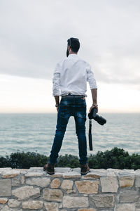 Rear view of man standing on retaining wall against sea