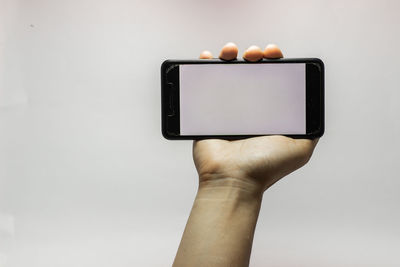 Close-up of hand holding mobile phone over white background