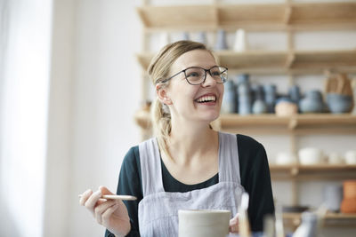 Smiling young woman looking up while learning pottery in art studio