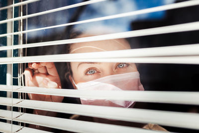 Close-up portrait of young woman seen through window