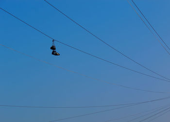 Low angle view of shoes hanging power line against clear blue sky
