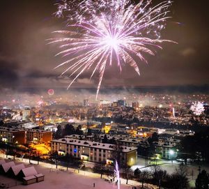 Firework display in city against sky at night