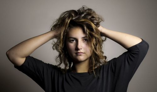 Portrait of young woman with hand in hair against gray background