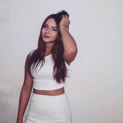 Portrait of smiling young woman with hand in hair standing against white background